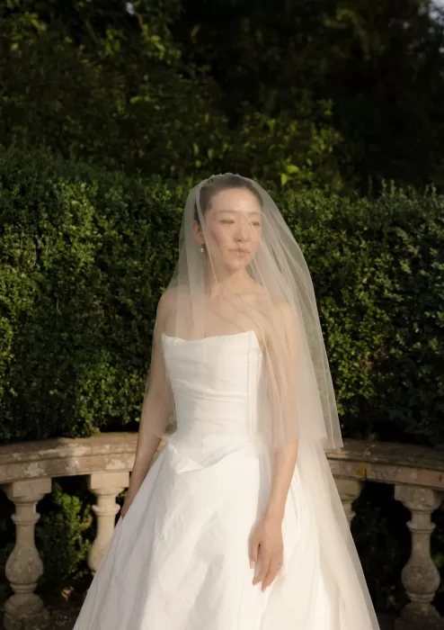The bride stands in golden sunlight at Manor House, her veil softly framing her serene expression.