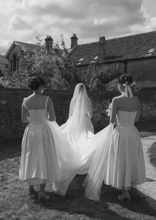 Bridesmaids help arrange the bride’s flowing gown and veil before the ceremony at Manor House, captured in elegant black and white.
