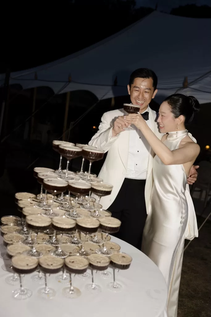 The bride and groom toast with espresso martinis beside a champagne tower under the Manor House night sky.