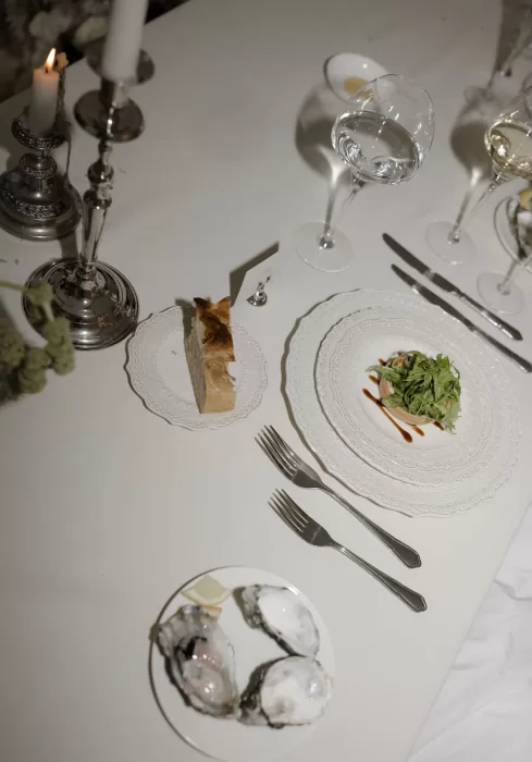 Refined dinner setting at Manor House featuring oysters, artisanal bread, and a plated salad course under candlelight.