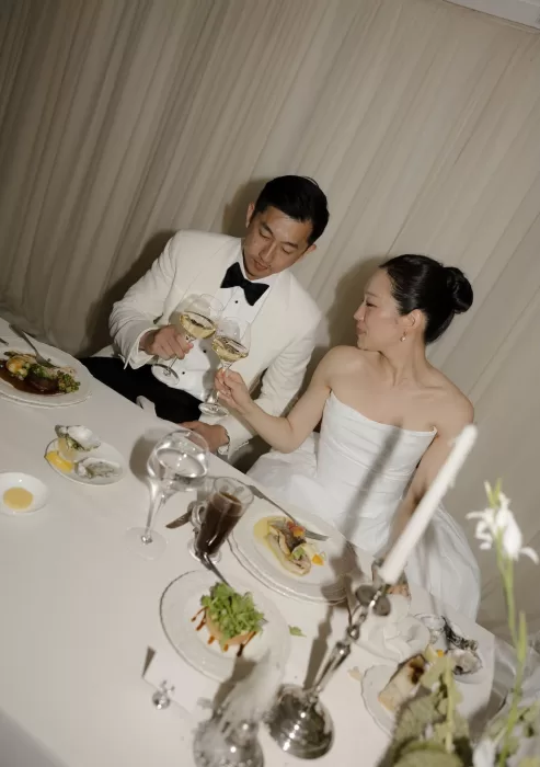 Bride and groom toast over an elegant dinner table at Manor House, surrounded by soft candlelight and fine details.