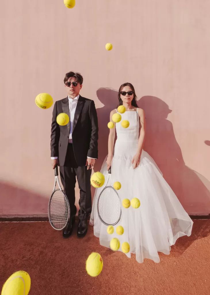 Bride and groom in sunglasses hold tennis rackets as yellow balls float mid-air at Neuendorf House.