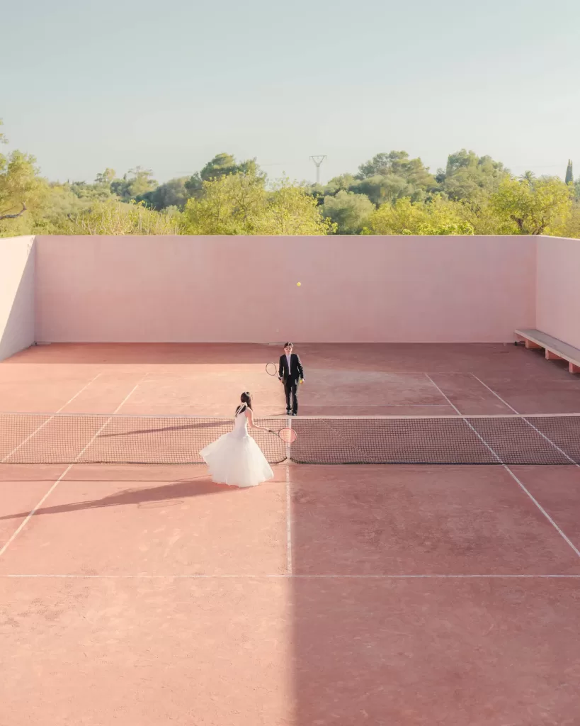 Bride and groom rally on the terracotta tennis court of Neuendorf House surrounded by modern architecture.
