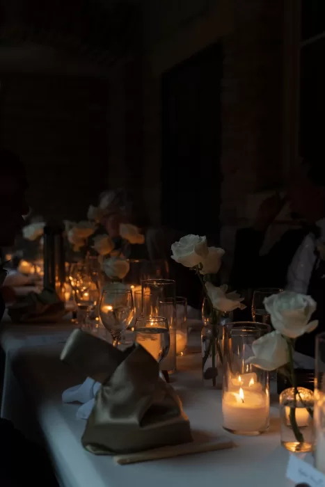 Candlelight flickers over white roses and glassware at an intimate evening dinner inside The Plummer House.