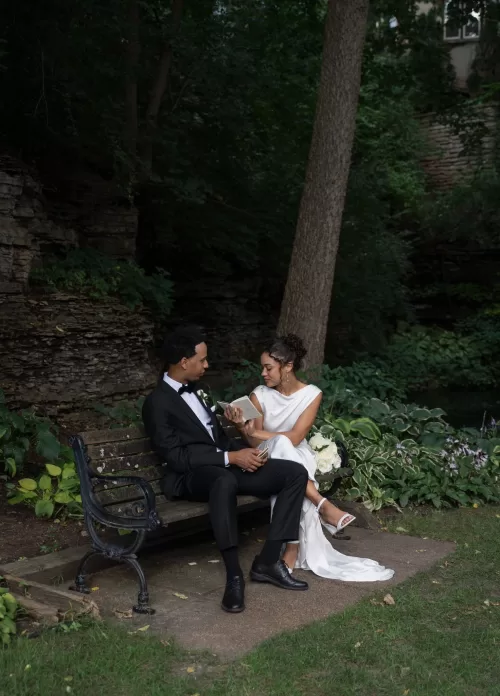 Bride reads her vows to the groom on a wooden bench surrounded by greenery at The Plummer House.
