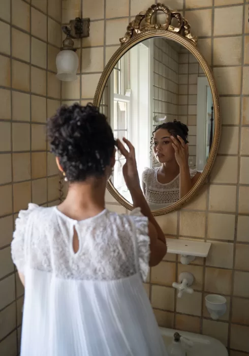 Bride touches up her curls while gazing into a vintage gold mirror at The Plummer House.