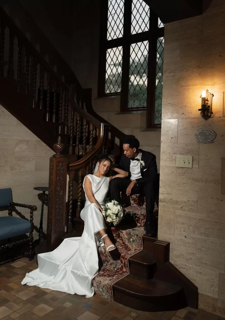Couple seated on the grand staircase sharing a quiet moment surrounded by warm light at The Plummer House.