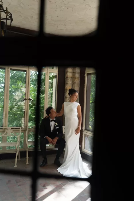 Bride and groom share a quiet moment by tall windows filled with greenery at The Plummer House.