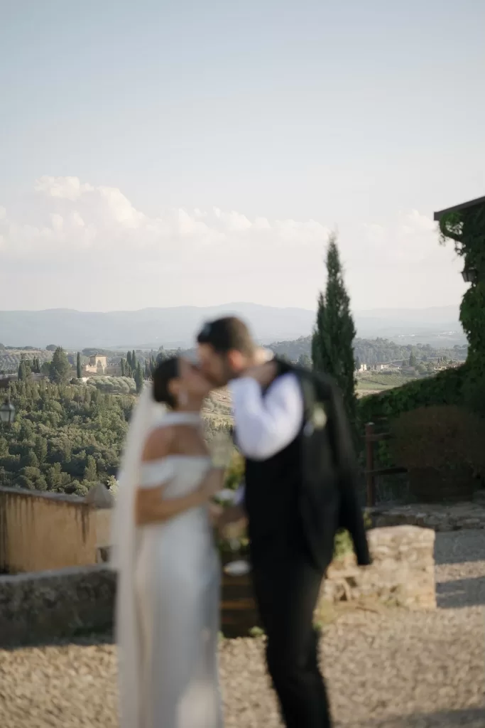 Softly blurred photograph of the couple kissing with the Tuscan landscape behind them at Quercia al Poggio.