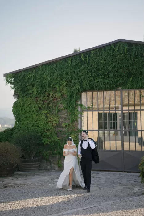 Bride and groom walking hand in hand outside the ivy-covered building at Quercia al Poggio.