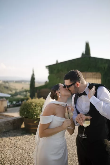 Newlyweds sharing a celebratory kiss with glasses of prosecco in the courtyard at Quercia al Poggio.