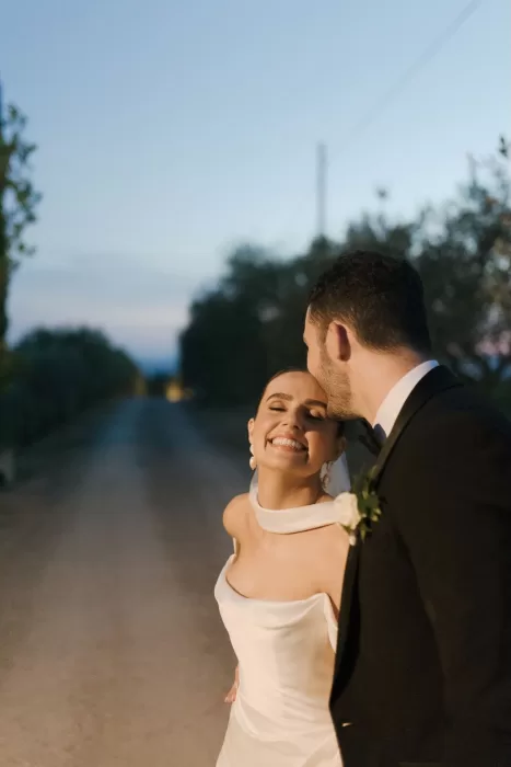 Groom kissing bride’s forehead at sunset on a quiet Tuscan road at Quercia al Poggio.