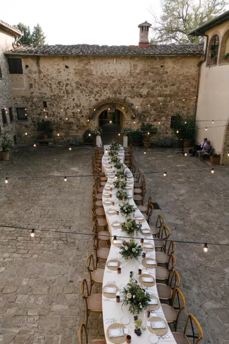 Long dinner table set for an outdoor wedding reception in the stone courtyard at Quercia al Poggio.