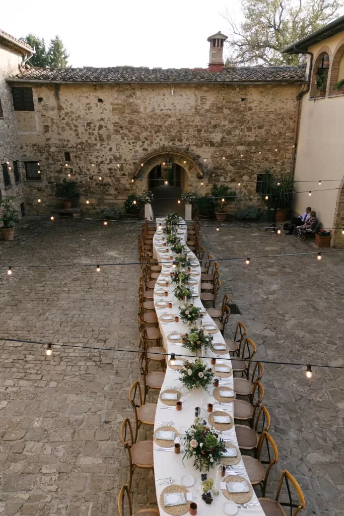 Long dinner table set for an outdoor wedding reception in the stone courtyard at Quercia al Poggio.