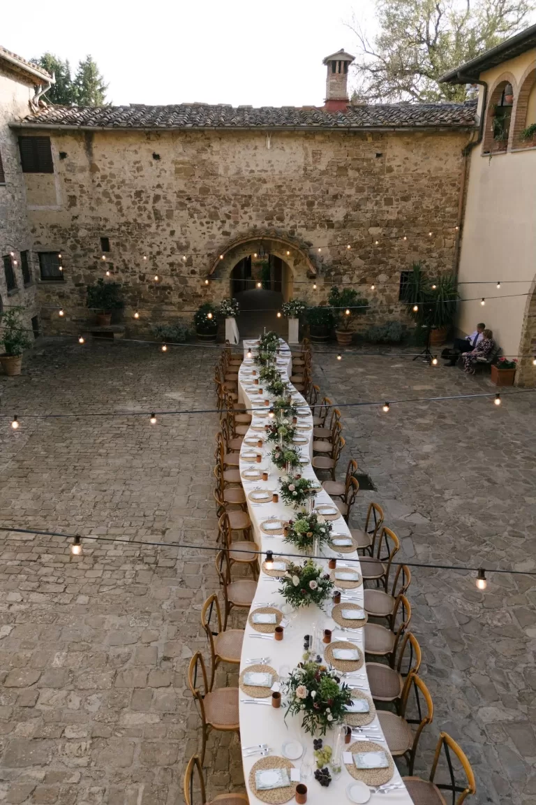 Long dinner table set for an outdoor wedding reception in the stone courtyard at Quercia al Poggio.