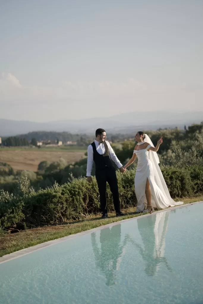 Bride and groom laughing by the pool at Quercia al Poggio with the Tuscan hills reflected in the water.
