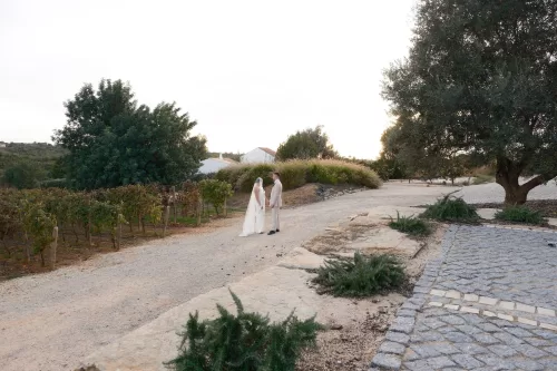 Couple holding hands on a sunlit path overlooking the vineyards and countryside at Quinta Dos Santos.