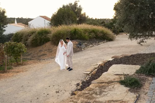 Bride and groom stroll along a rustic garden path framed by olive trees at Quinta Dos Santos.