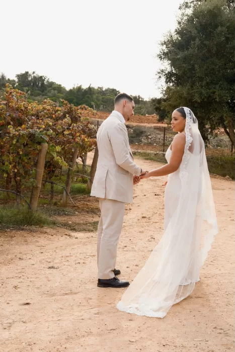 Bride and groom holding hands among the vineyard rows at Quinta Dos Santos, captured in soft golden light