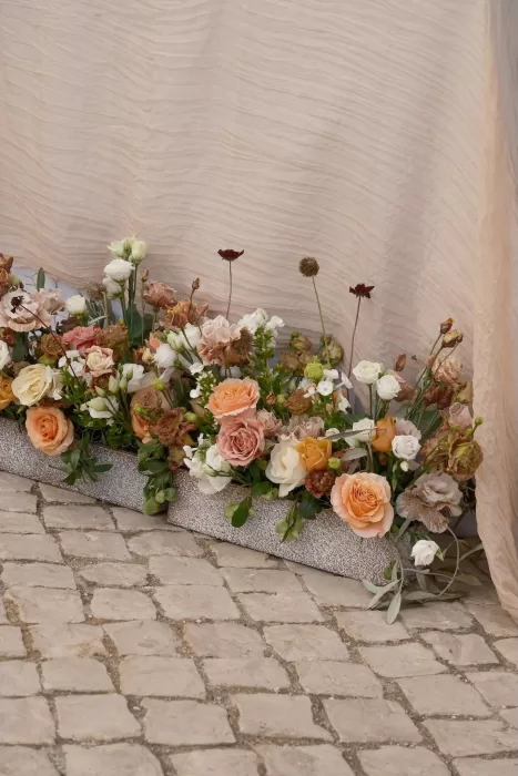 Romantic blush and apricot floral arrangements at Quinta Dos Santos styled against textured fabric and cobblestone flooring.