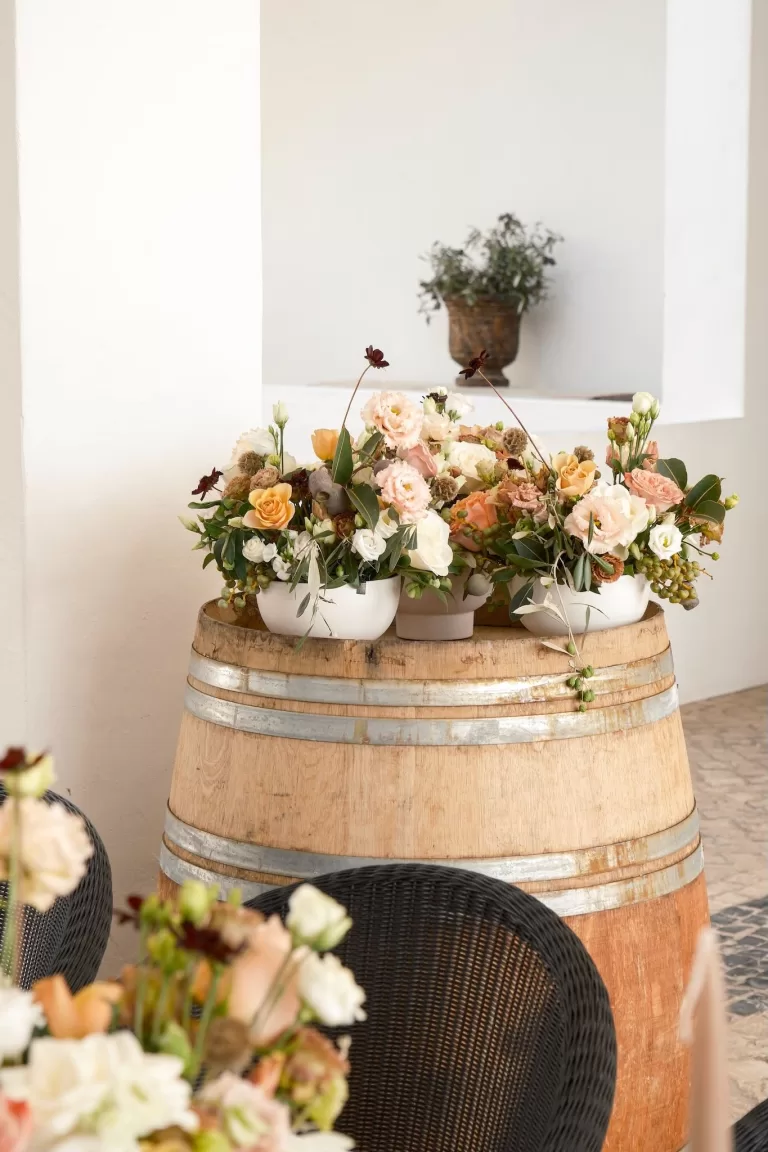 Lush floral arrangements in white ceramic vases displayed on a rustic wine barrel at Quinta Dos Santos.