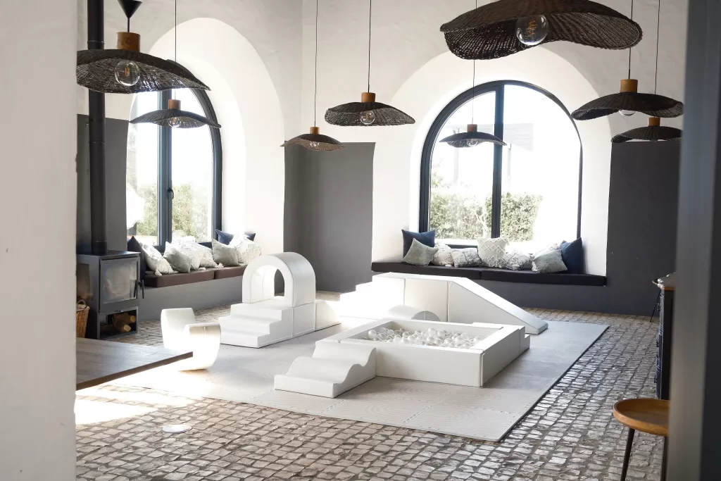 Modern lounge space at Quinta Dos Santos with arched windows, woven light fixtures, and neutral play area.