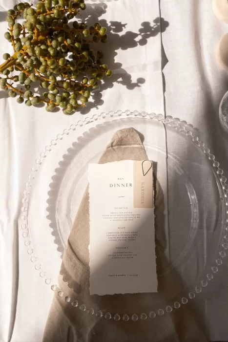 Elegant wedding menu placed on a glass charger with linen napkin and olive branch detail at Quinta Dos Santos.