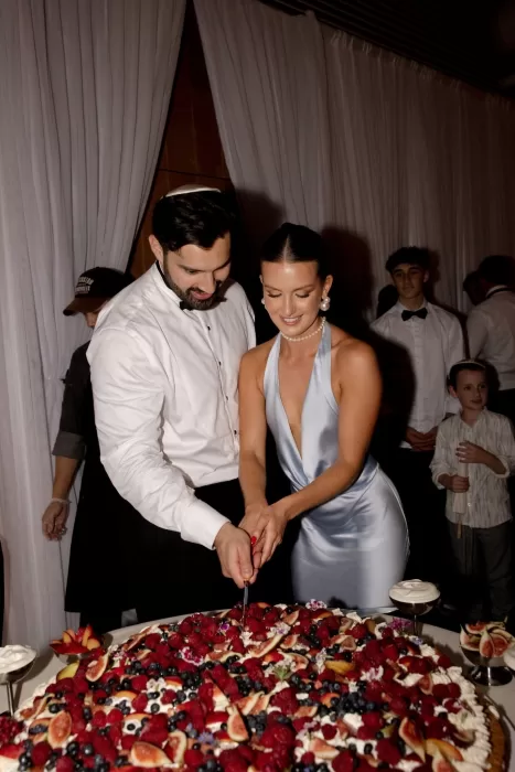 Couple cutting fruit-topped wedding cake at Sergeants Mess reception.