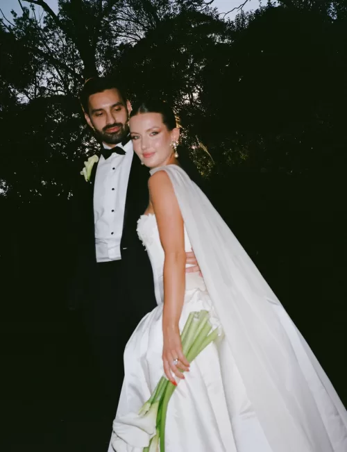 Bride and groom embracing outdoors, bride holding white calla lilies at Sergeants Mess.