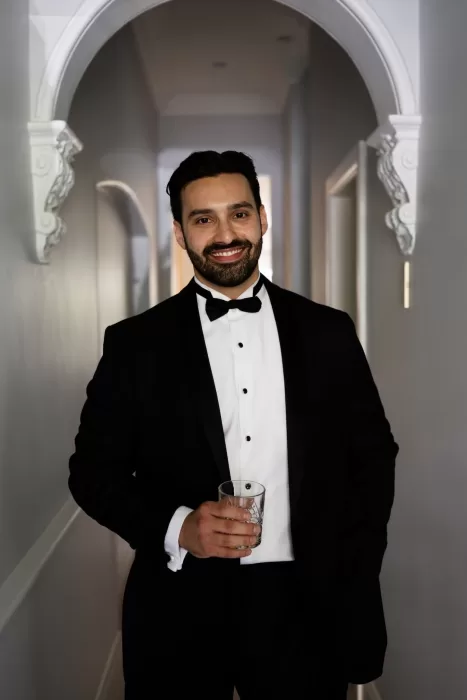 Groom in black tuxedo with bow tie smiling in hallway at Sergeants Mess wedding.
