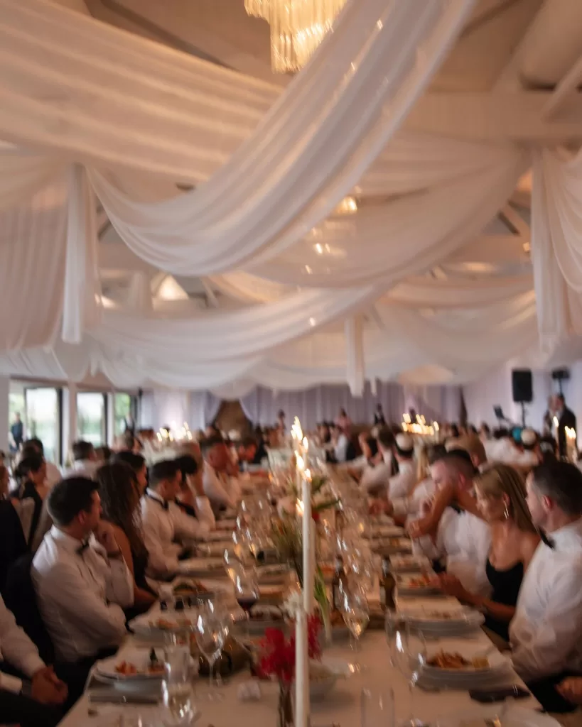 Guests seated along candlelit banquet tables under white drapery at Sergeants Mess wedding.
