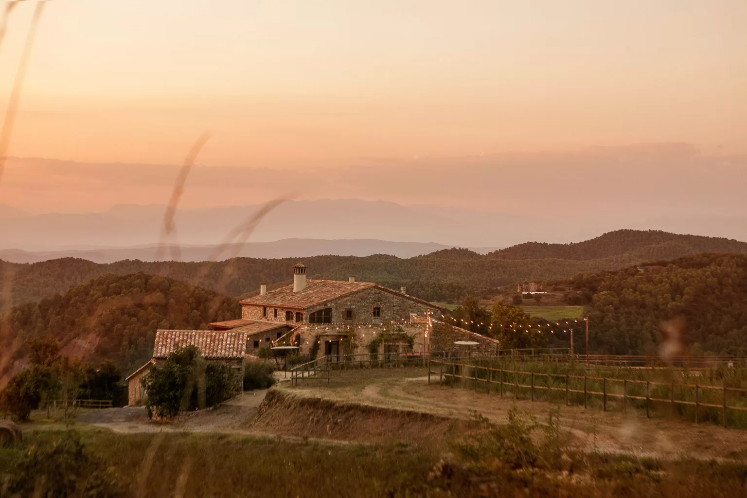 Distant view of This Must Be The Place at dusk, nestled in rolling Catalan hills with string lights glowing.