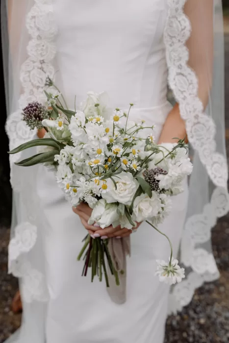 Bride holding a white and green bouquet with chamomile flowers at This Must Be The Place wedding.