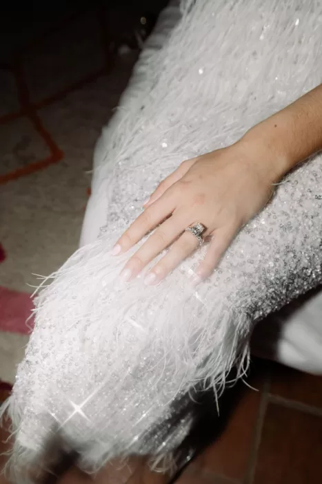 Close-up of the bride’s hand resting on a feathered sequin dress, showing her elegant engagement ring.
