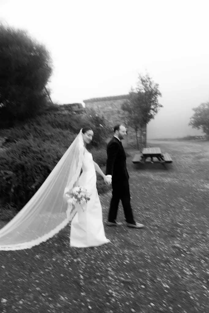 Bride and groom walking hand in hand through the misty grounds of This Must Be The Place, captured in motion.