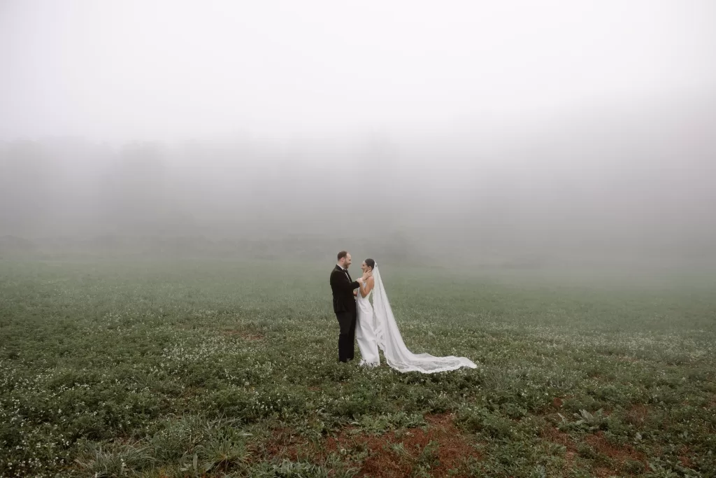 Bride and groom standing in a fog-covered field at This Must Be The Place, sharing a quiet moment together.