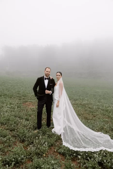 Bride and groom standing together in a fog-covered field at This Must Be The Place, exuding quiet elegance.