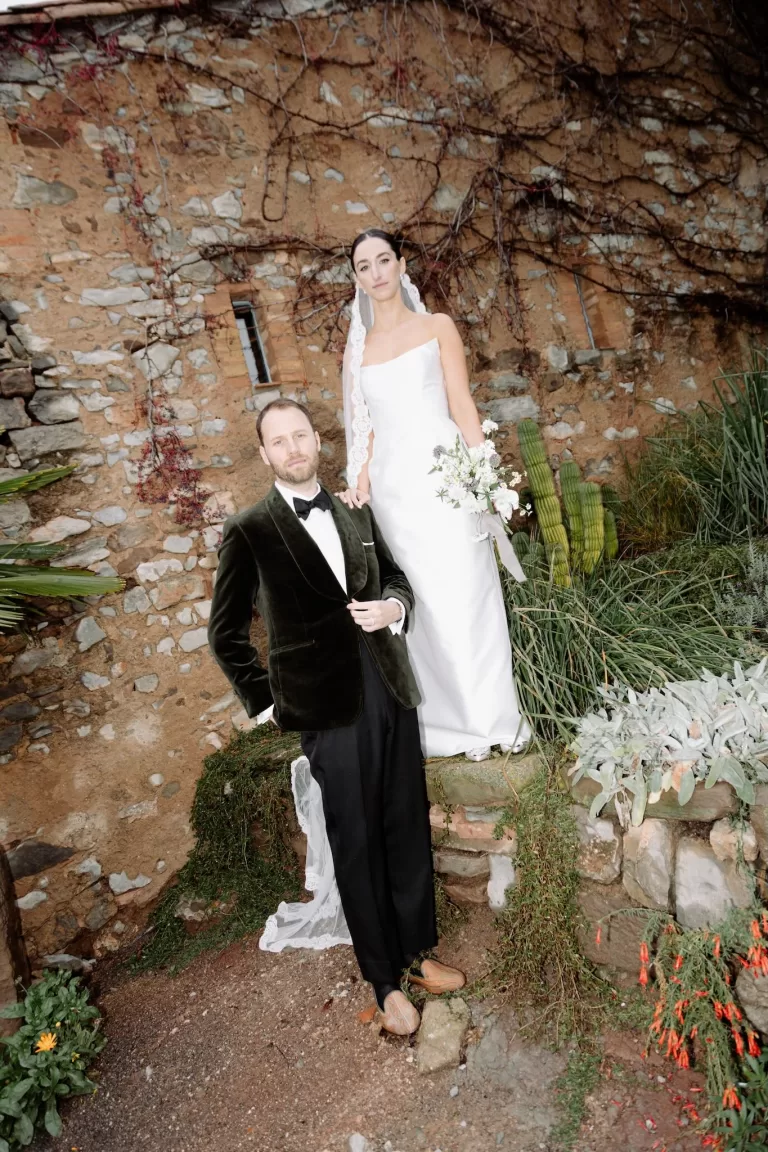 Bride and groom posing elegantly by a rustic stone wall at This Must Be The Place wedding venue.