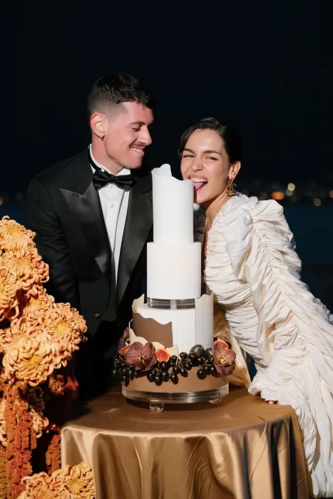 Newlyweds laughing beside a sculptural wedding cake adorned with figs and orchids at Villa Balbiano.