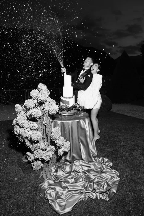Black and white photo of couple popping champagne beside the wedding cake at Villa Balbiano.