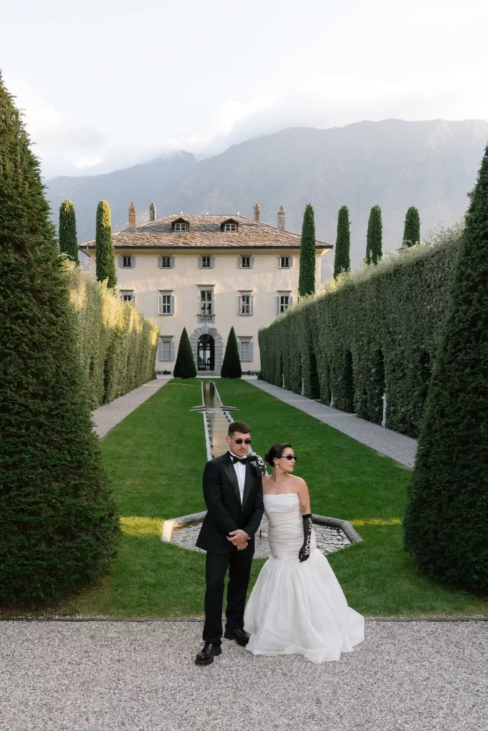 Stylish bride and groom posing in Villa Balbiano’s formal gardens framed by cypress trees.