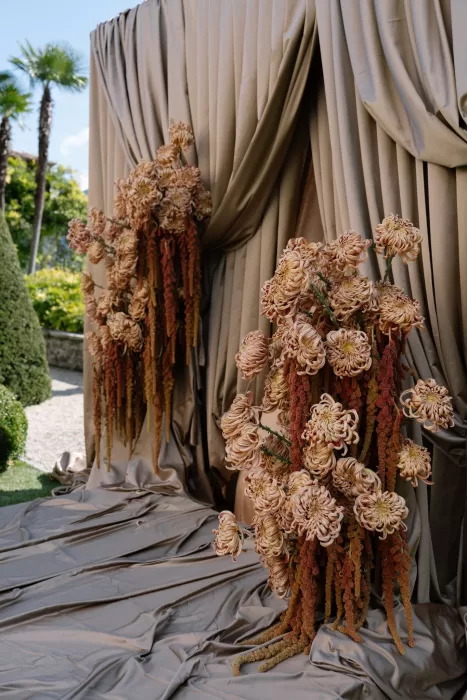 Dramatic floral arrangement of warm-toned blooms against bronze drapery at Villa Balbiano.