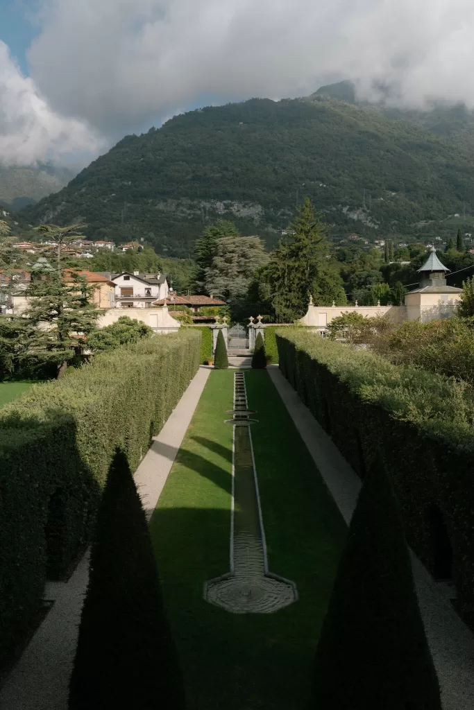 Aerial view of manicured hedges and garden fountain framed by mountains at Villa Balbiano.