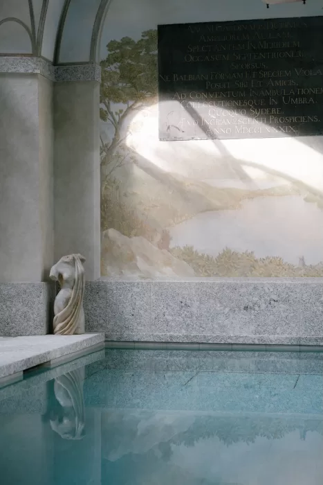 Indoor pool with marble statue and frescoed wall art bathed in soft light at Villa Balbiano.