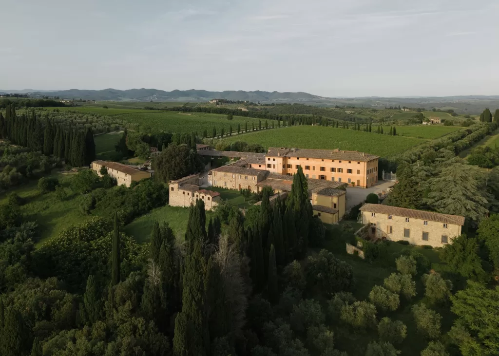 Aerial panorama of Villa Catignano and surrounding Tuscan vineyards and cypress-lined roads at golden hour.