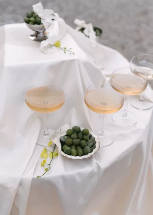 Softly styled detail of champagne coupes and a bowl of green olives on white fabric at Villa Catignano.