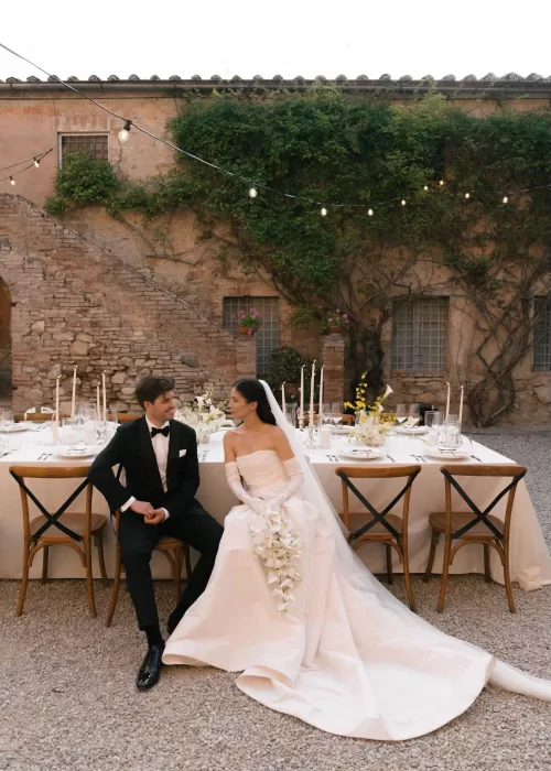 Bride and groom share a quiet moment beside an elegant dinner table in the rustic courtyard of Villa Catignano, framed by ivy and string lights.
