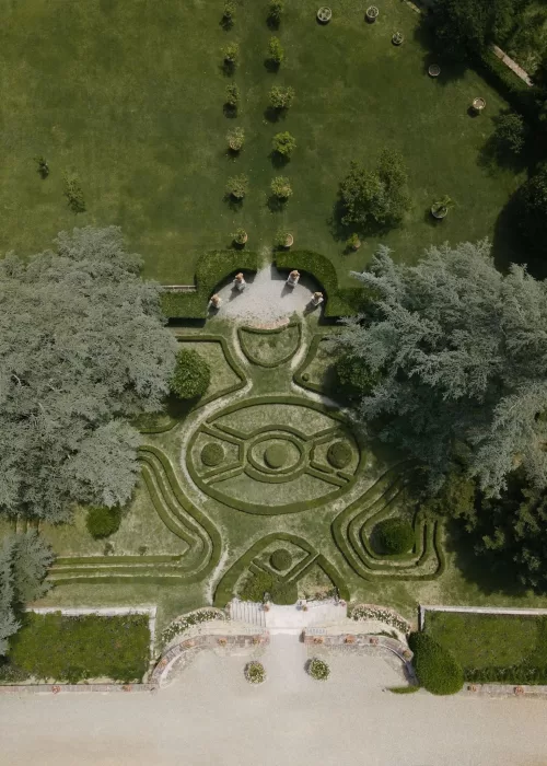 Aerial view of Villa Catignano’s formal Italian garden with symmetrical hedges and statues surrounded by lush greenery.