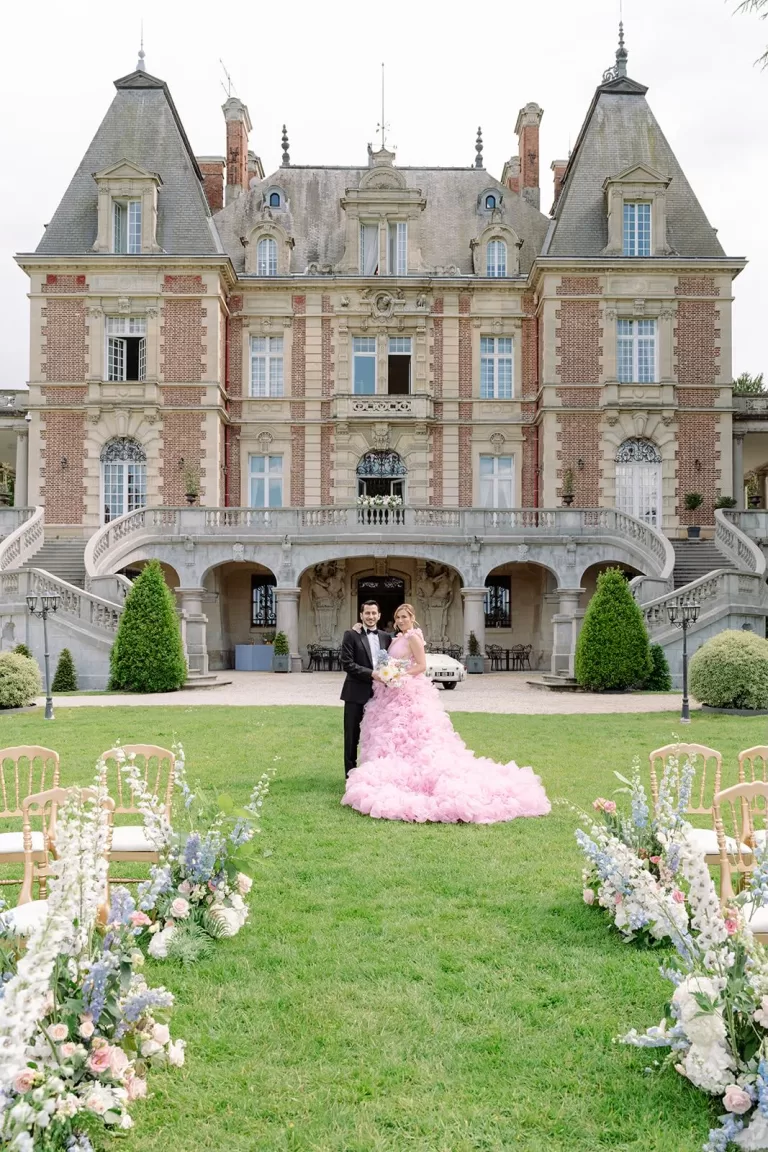 Couple posing on the lawn at Château Bouffémont with the château’s sweeping stone staircases and façade behind them.