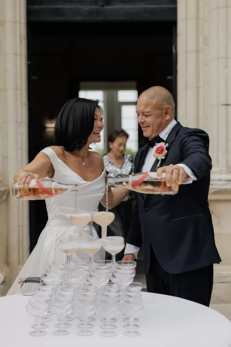 Couple pouring champagne into a glass tower during their wedding celebration at Château de Jalesnes.